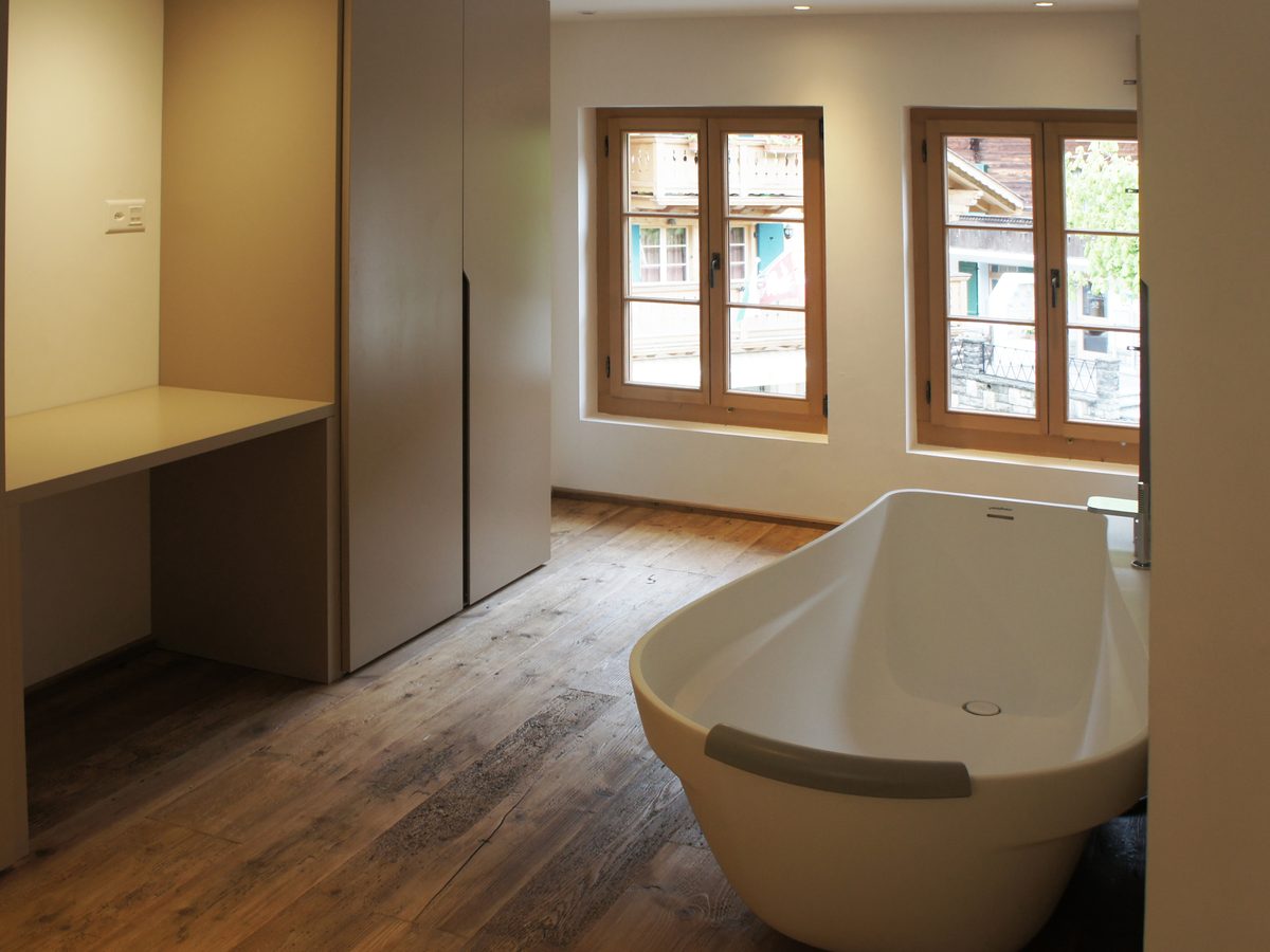 Salle de bains d'un appartement du chalet de Rougemont : baignoire îlot, plancher en vieux bois et fenêtres de chalet